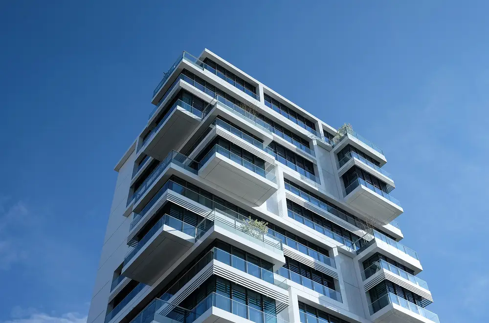 Ein modernes, mehrstöckiges Wohnhaus mit großen Glasfenstern und versetzten Balkonen, verwaltet von einer professionellen Immobilienverwaltung, vor einem strahlend blauen Himmel.